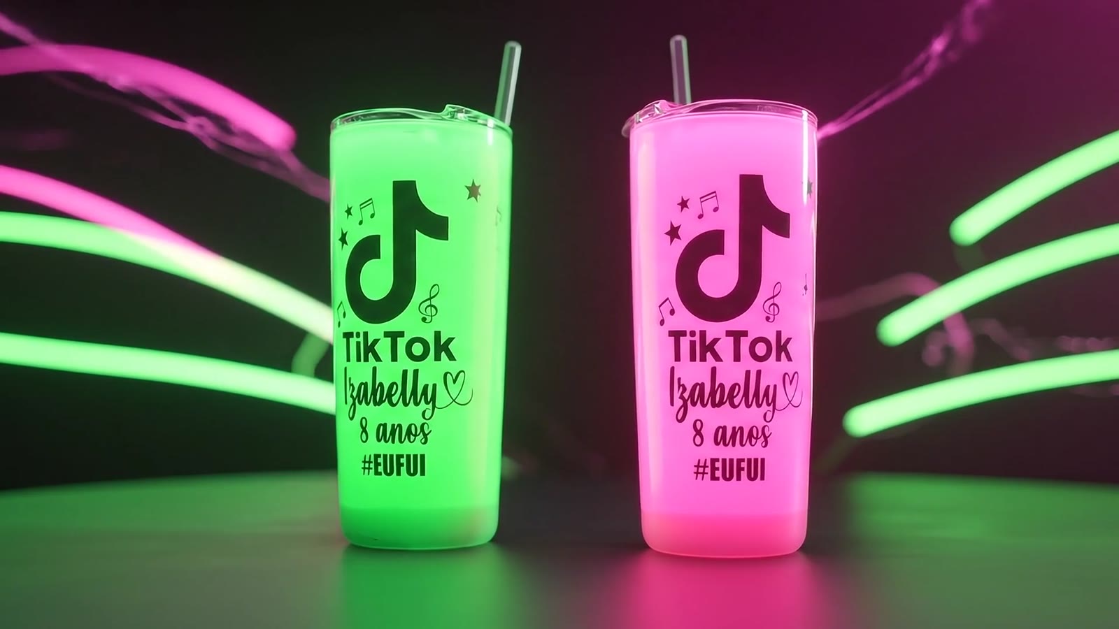 Dois copos personalizados, verde e rosa, iluminados por luzes neon sobre fundo escuro.